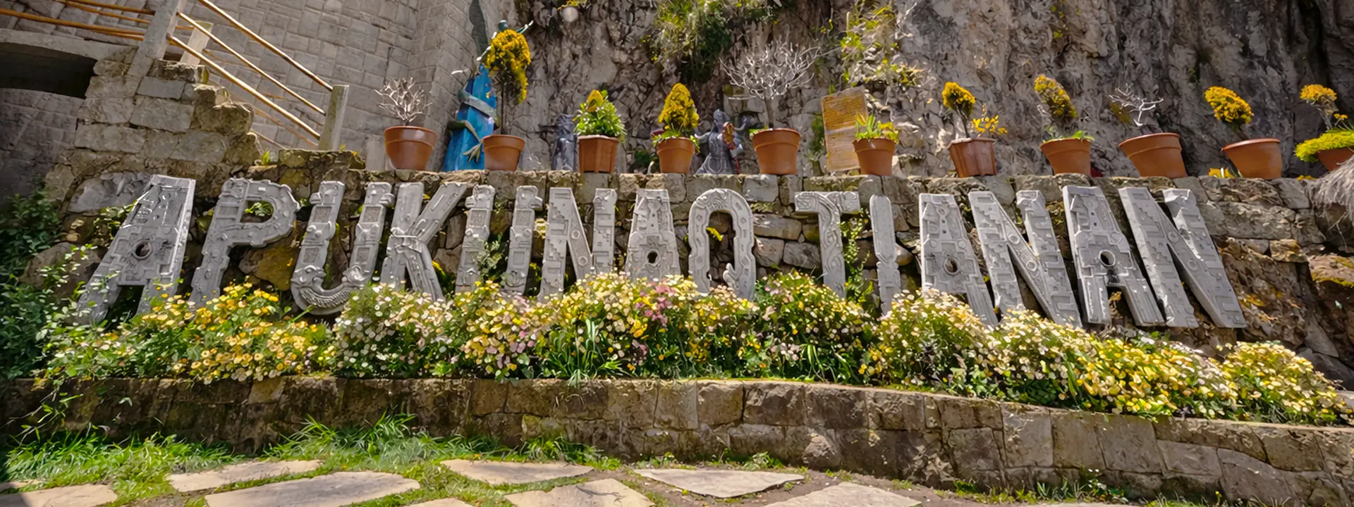 Vista exterior de Apukunaq Tianan con estructura de madera, muro de piedra y escultura de rostro tallada en la roca.
