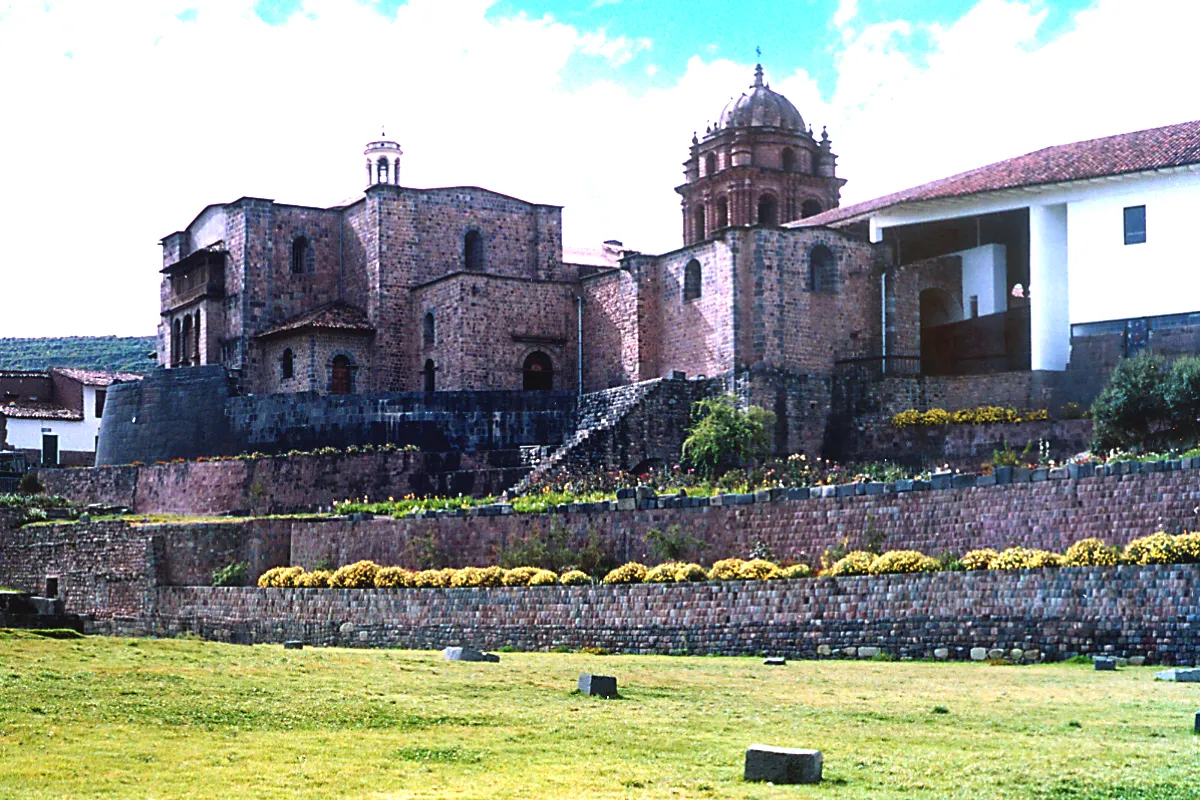 Vista del Coricancha y el Convento de Santo Domingo en Cusco, con muros incas, andenes de piedra y la cúpula colonial al fondo.