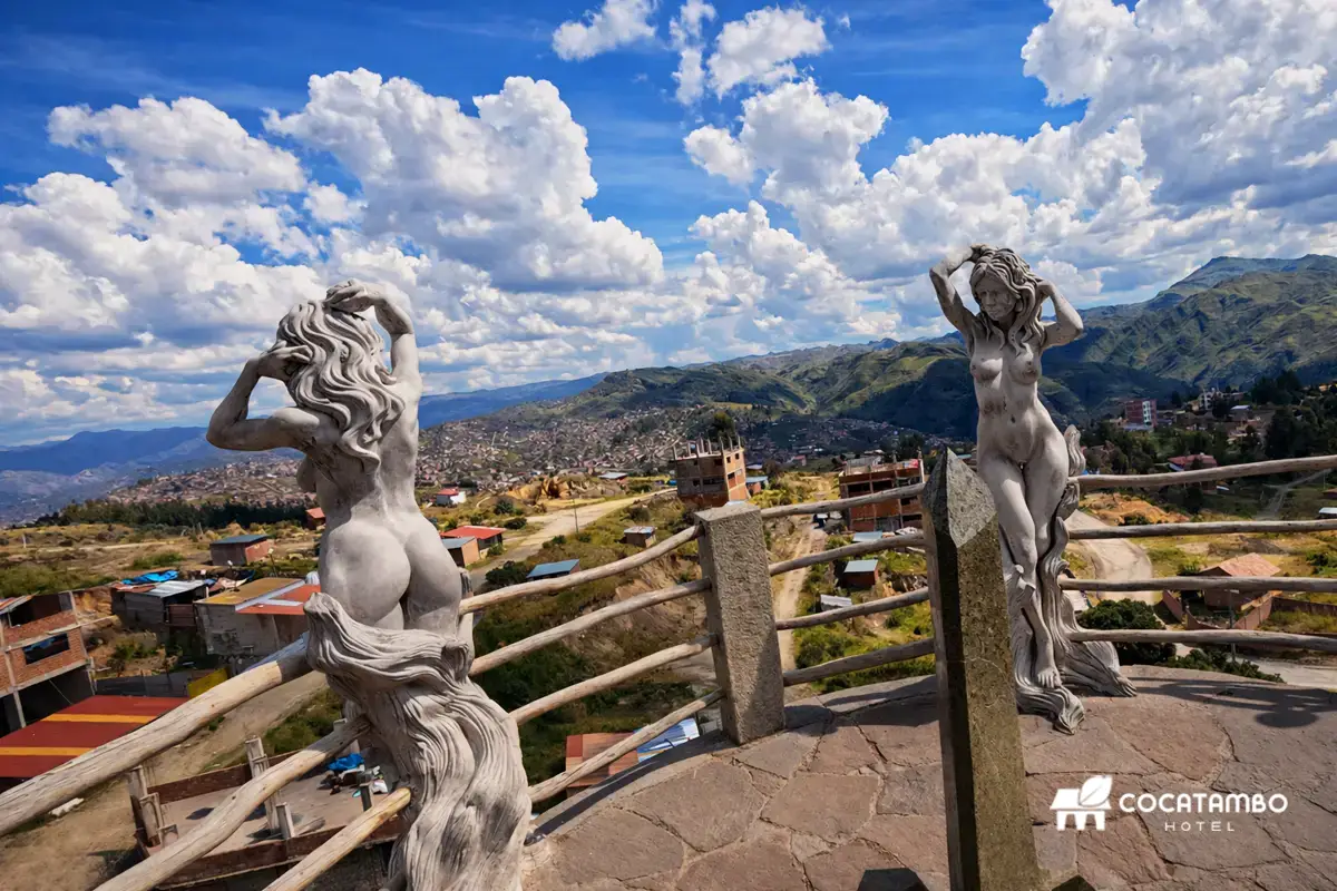 Esculturas de las Acllas sobre un mirador de piedra con vista panorámica de montañas, cielo nublado y paisaje urbano andino.