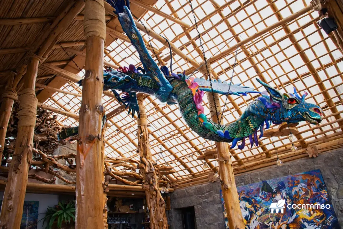 Escultura de Amaru suspendida del techo en el interior del Restaurante de madera con columnas y pinturas.