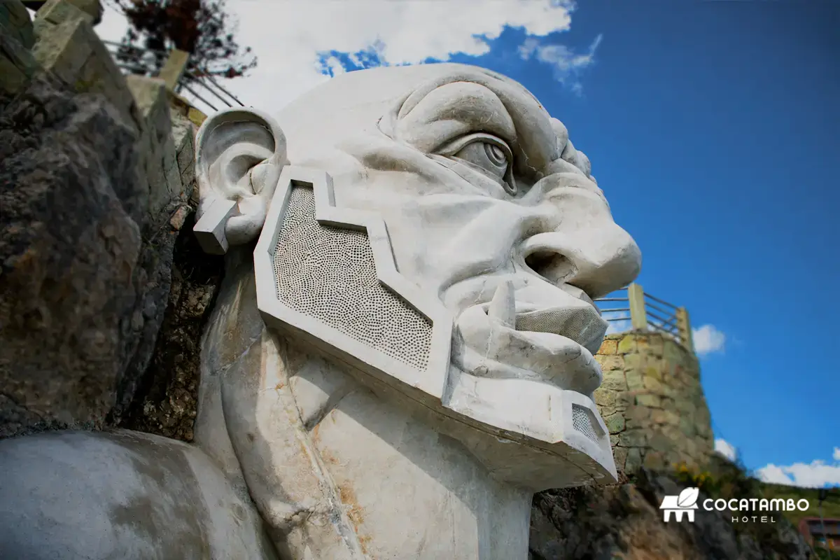 Primer plano de una escultura monumental de rostro blanco con gran orejera geométrica.