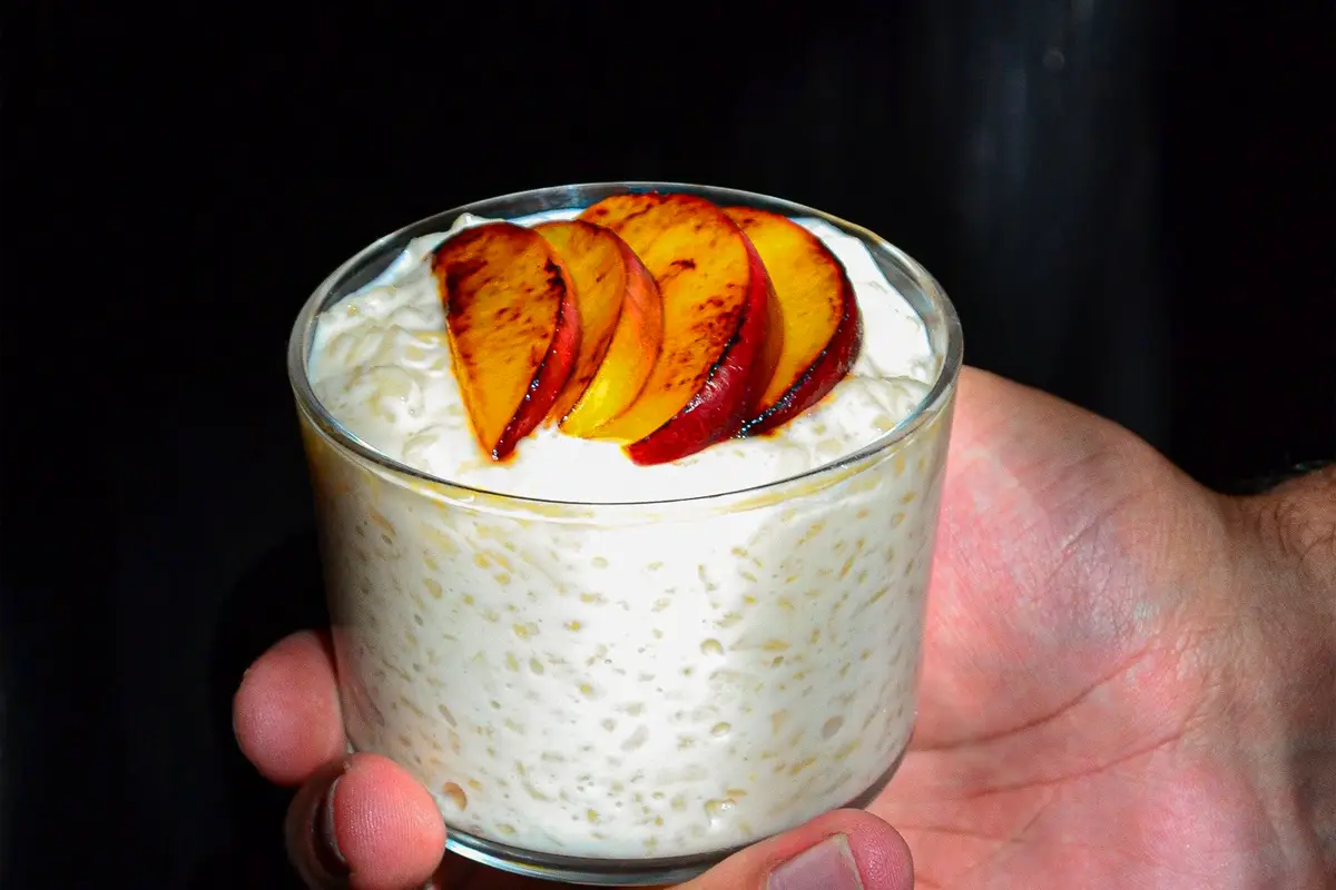 Arroz con leche en vaso, decorado con láminas de durazno encima.