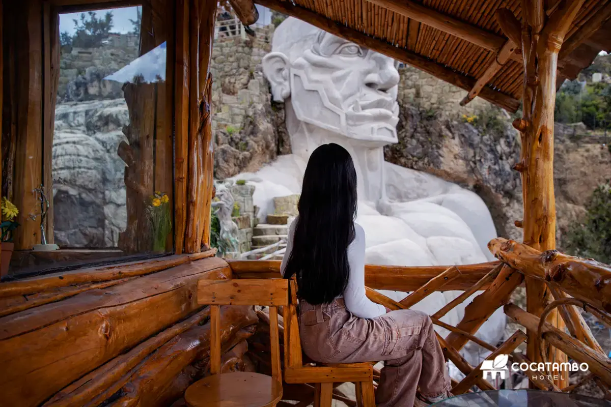 Mujer sentada en balcón rústico de Mujer sentada en balcón rústico de madera del cafetin observando una escultura monumental blanca tallada en la montaña.observando una escultura monumental blanca tallada en la montaña.