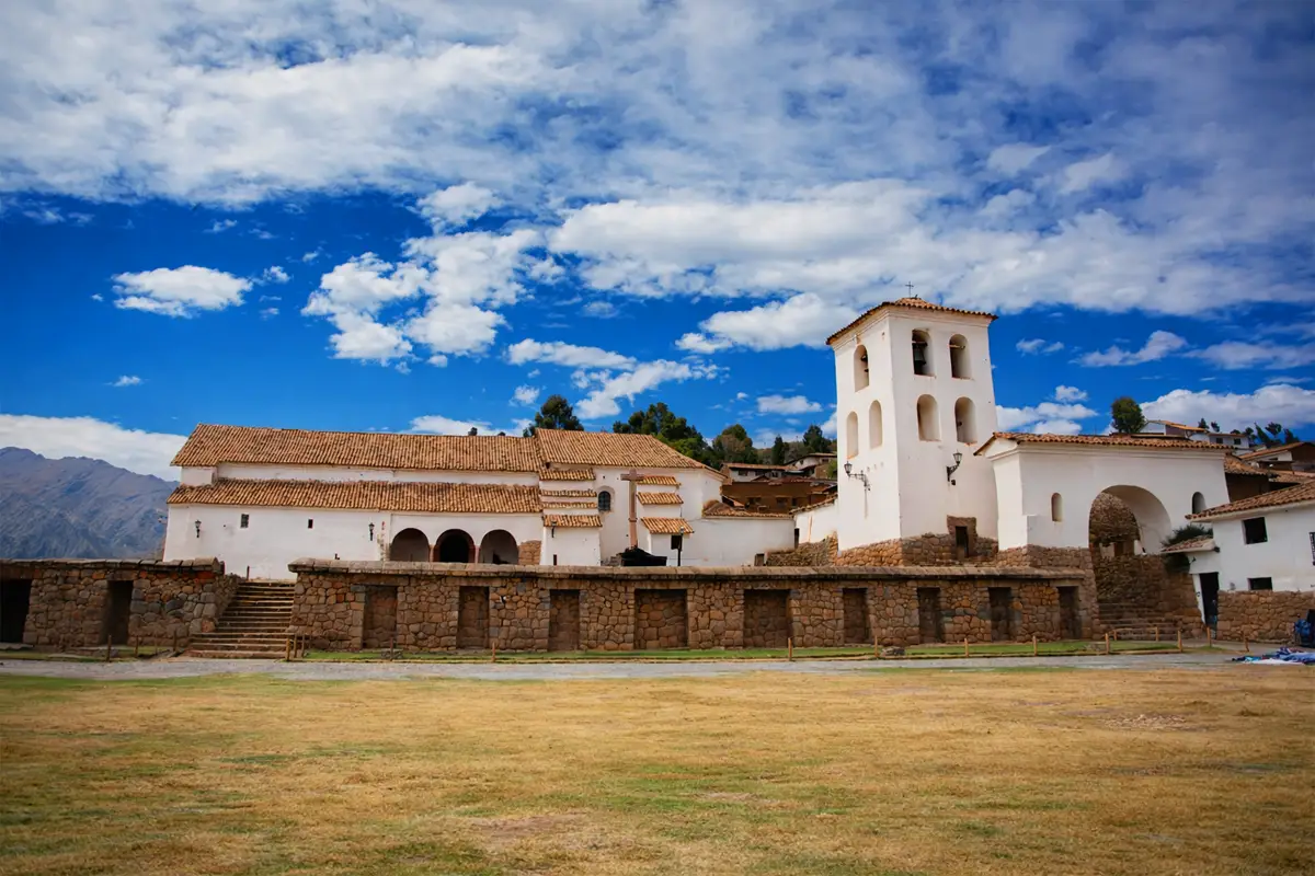 Iglesia colonial de Chinchero con torre campanario, muros de piedra y cielo azul con nubes en Cusco