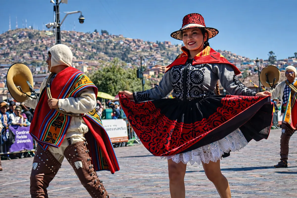 Pareja de bailarines de Cholo Qorilazo en plaza de Armas Cusco durante desfile folclórico con músicos tradicionales.