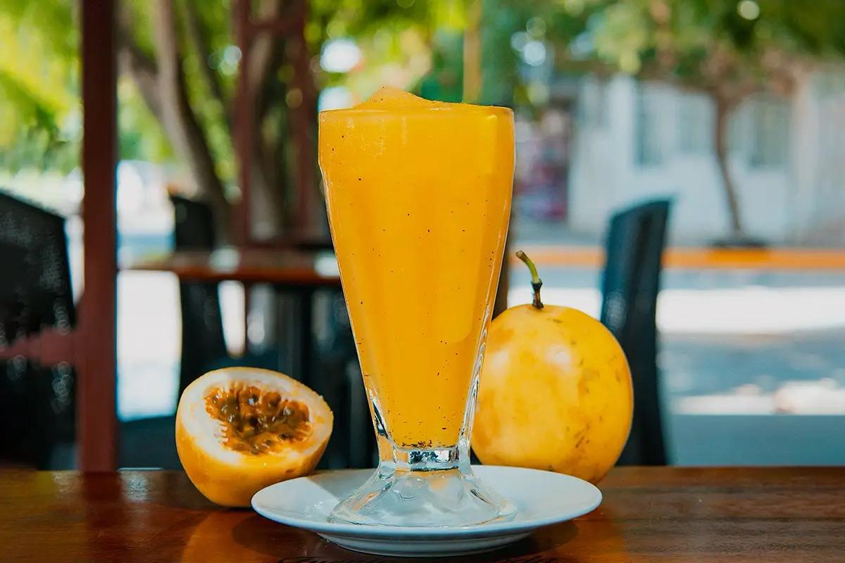 Cremolada de maracuyá en vaso alto, con fruta de maracuyá entera y partida al lado.