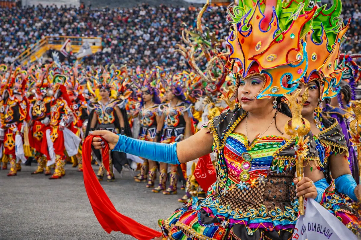 Comparsa de Diablada con trajes coloridos elaborados desfilando frente a una multitud en festival folclórico.