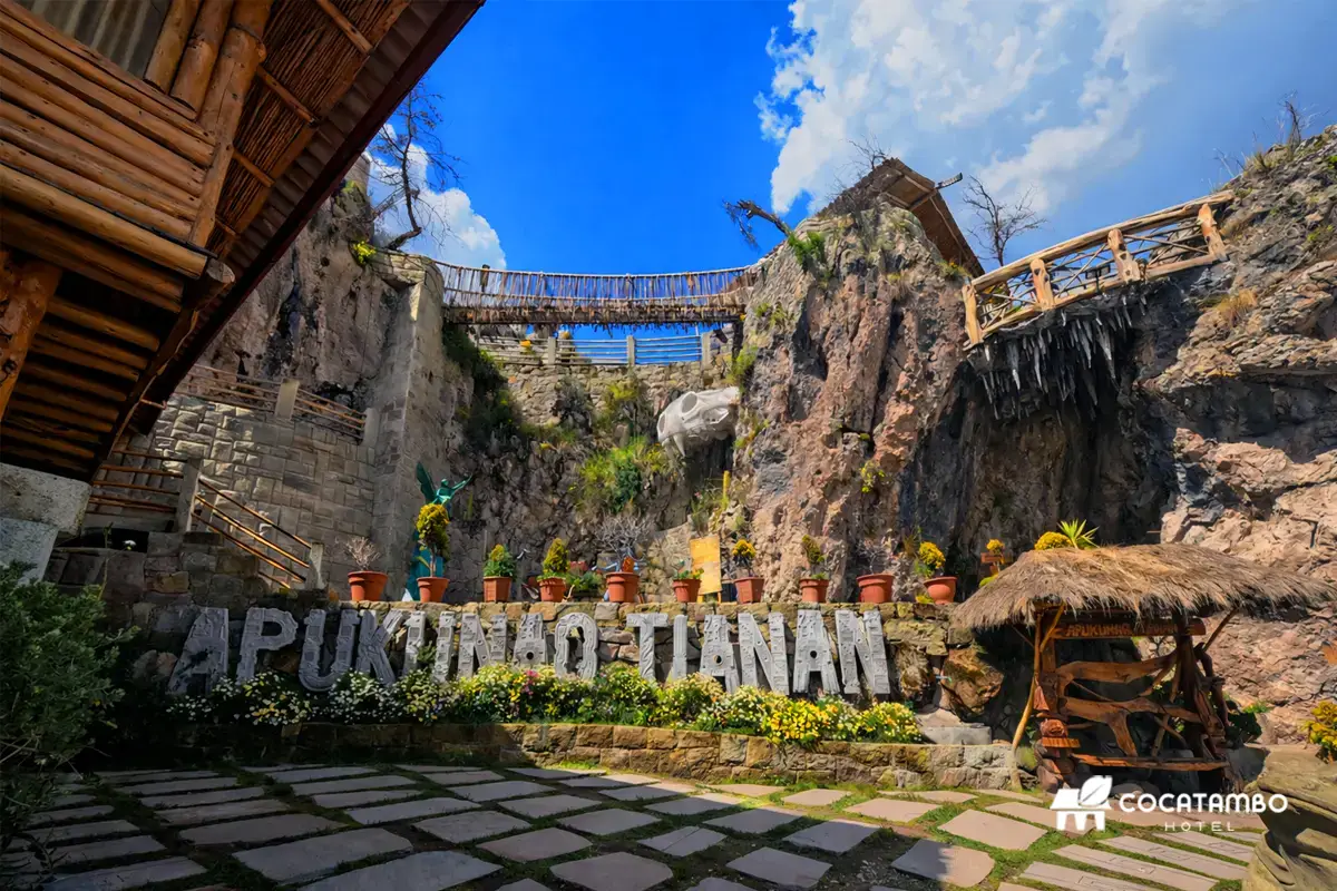 Vista amplia de Apukunaq Tianan con letrero monumental, patio de piedra, puentes elevados y paredes rocosas.