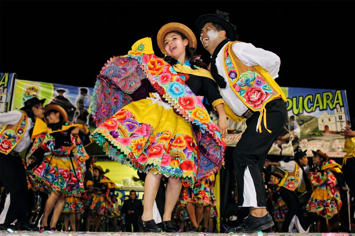 Pareja de danzantes con trajes bordados y colores intensos en escenario nocturno durante festival cultural.