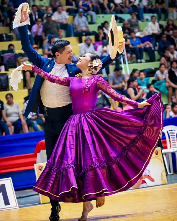 Pareja de bailarines de Marinera Norteña en escenario deportivo, con vestido morado y pañuelos en alto.