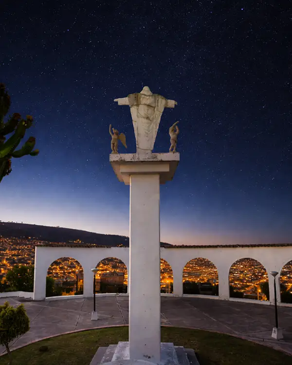 Monumento de Cristo sobre columna con vista panorámica de la ciudad al atardecer 