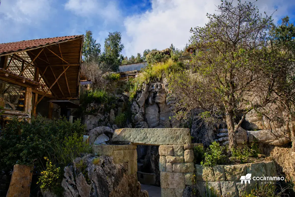 Vista exterior de Apukunaq Tianan con estructura de madera, muro de piedra y escultura de rostro tallada en la roca.