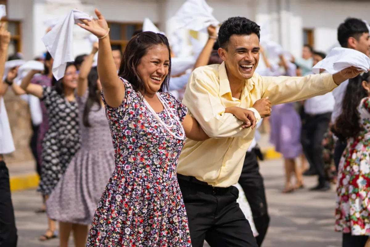 Pareja sonriendo y bailando Pandilla amazonica con pañuelos blancos durante celebración popular al aire libre.