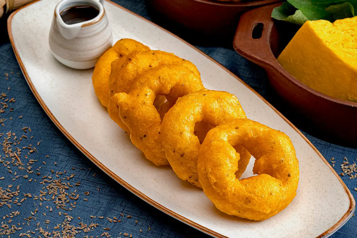 Picarones peruanos de zapallo y camote en plato alargado, listos para acompañar con miel.