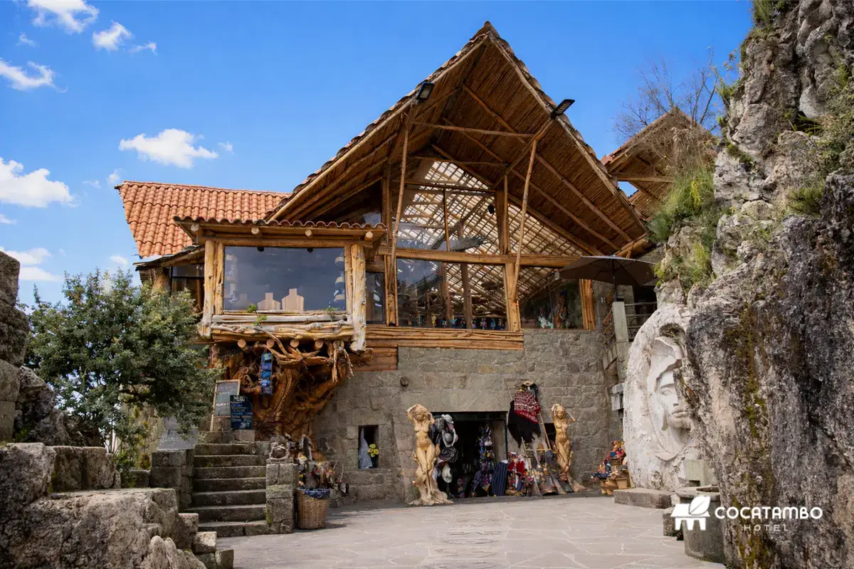 Fachada rústica de madera y piedra del Restaurante en Apukunaq Tianan, con techos andinos, escaleras y gran relieve tallado en roca.