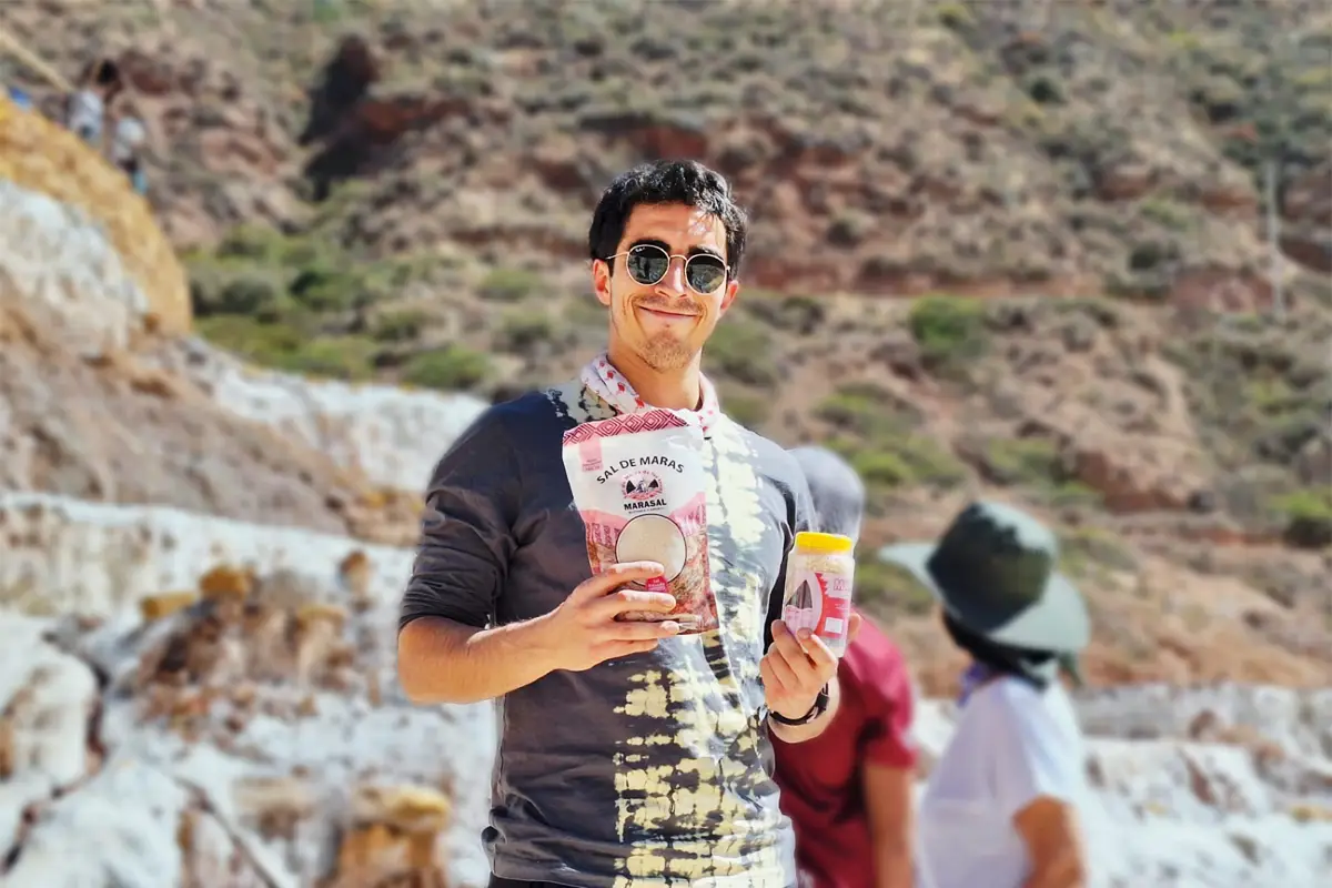 Turista sosteniendo productos de sal de Maras frente a las pozas de sal en Maras, Cusco