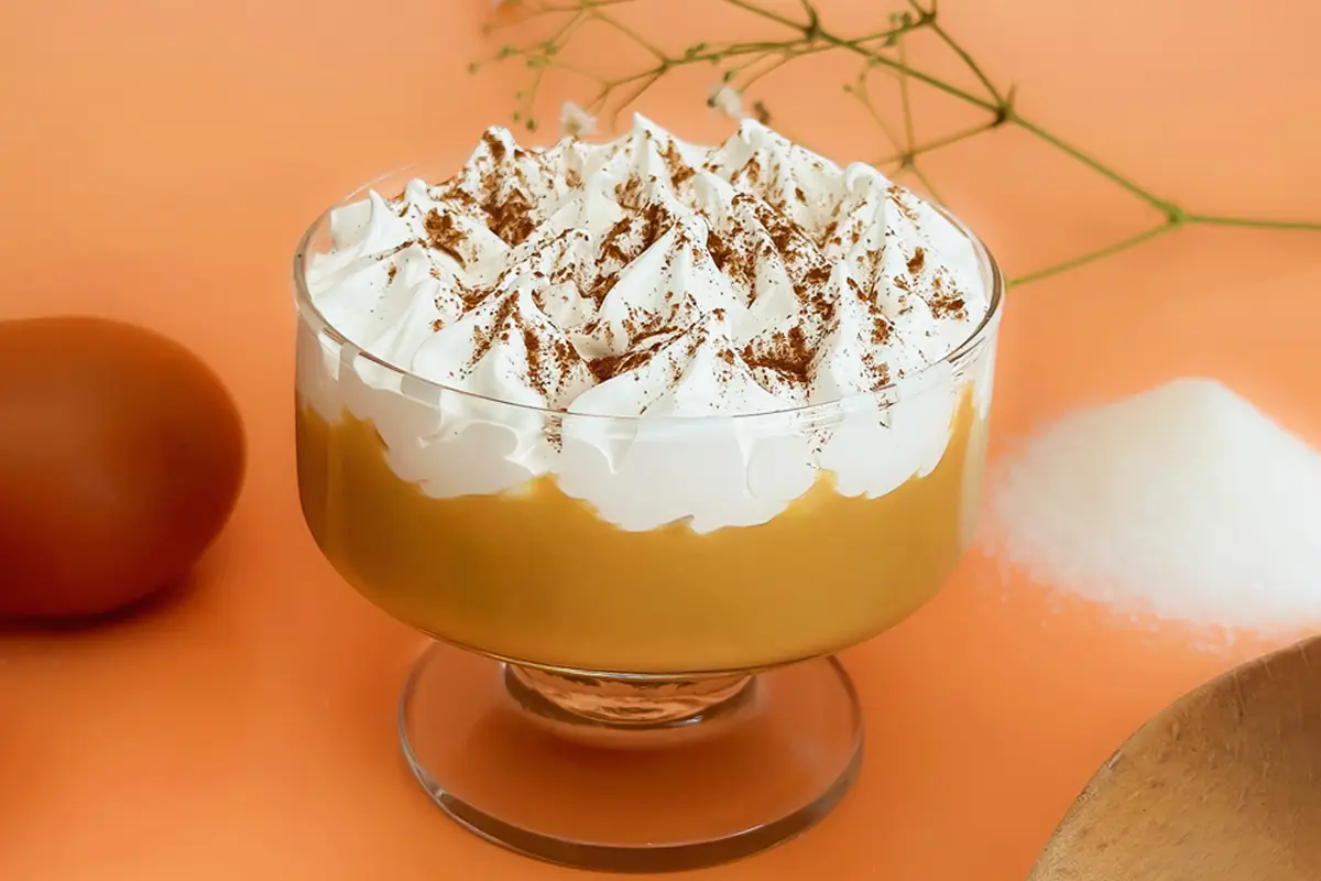 Suspiro a la limeña servido en copa, con merengue encima y canela espolvoreada.