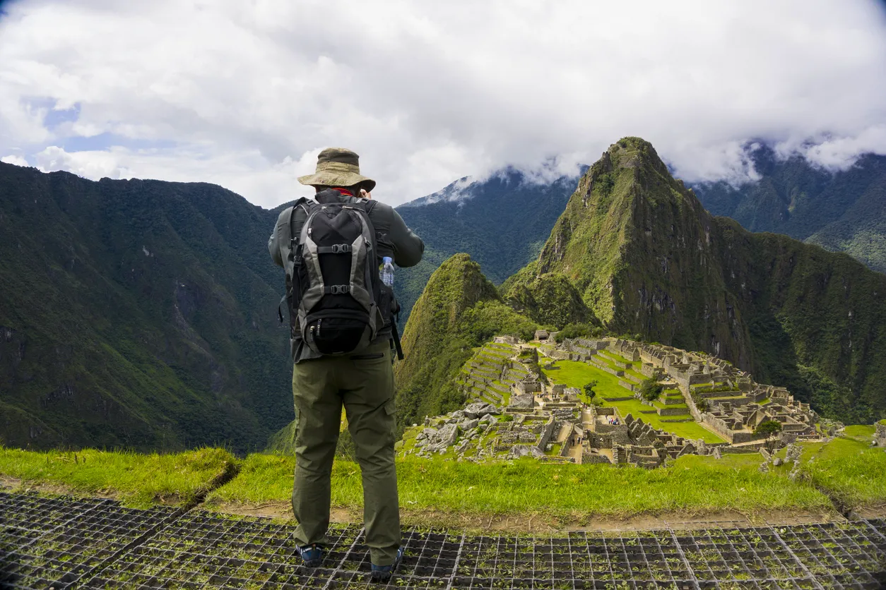 Turista observando la ciudadela de Machu Picchu desde el mirador con Huayna Picchu al fondo