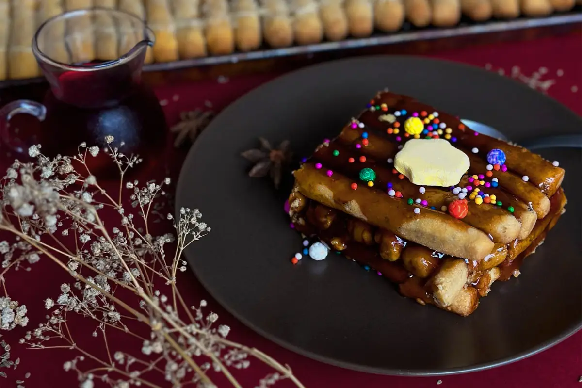 Turrón de Doña Pepa con miel y grageas de colores, servido en plato negro.